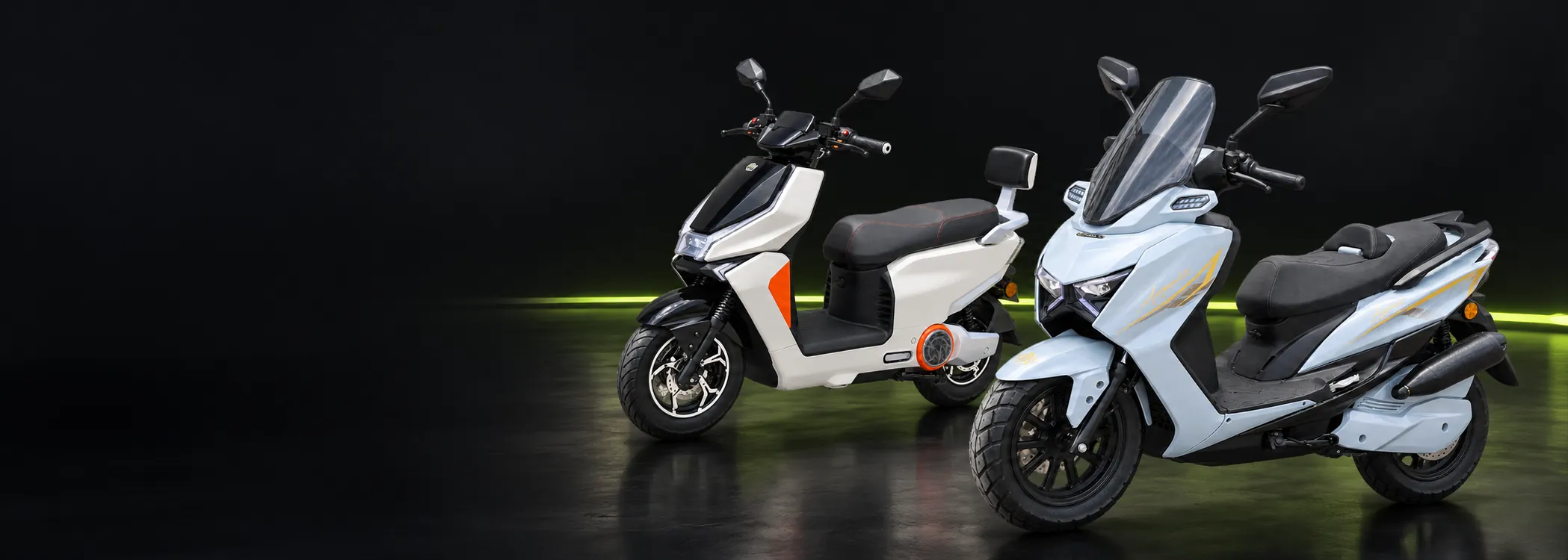 Duas scooters elétricas, uma branca e uma azul-clara, em estúdio escuro com faixa de luz verde